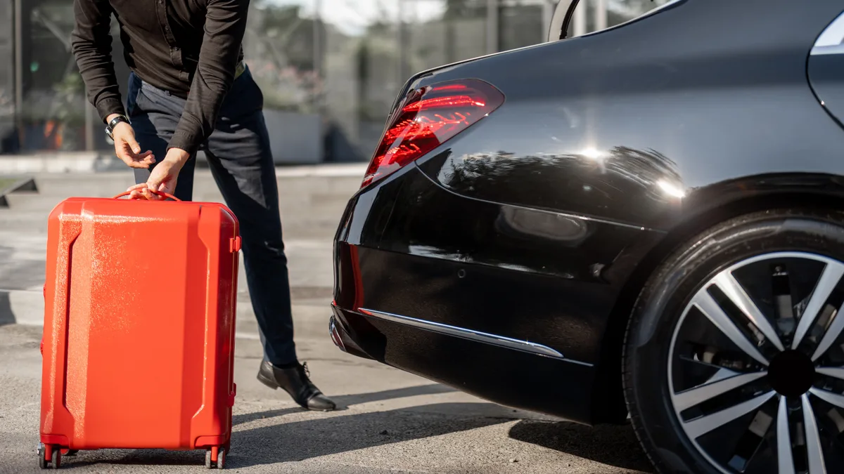 A traveller wheeling a suitcase to the boot of a sedan