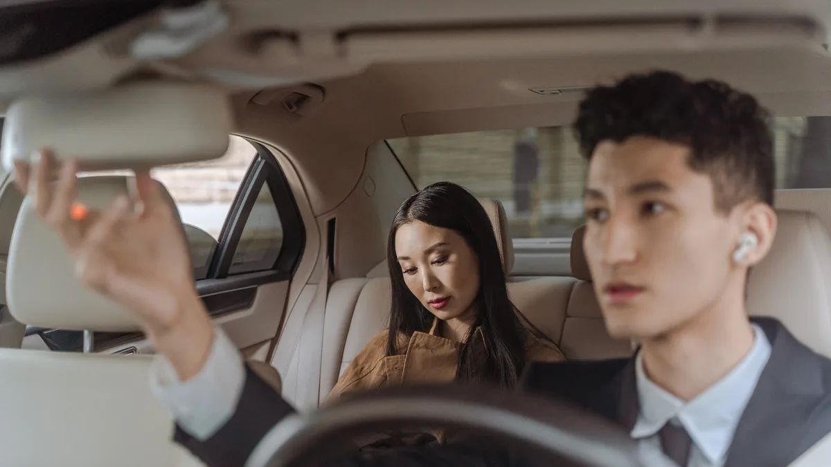 A chauffeur adjusting the rear-view mirror with a passenger seated behind